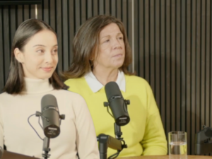 Leoni Boyle and Lucy Bailey sitting in the Working on Wellbeing podcast studio. They are both smiling and each sitting behind a black microphone.