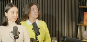 Leoni Boyle and Lucy Bailey sitting in the Working on Wellbeing podcast studio. They are both smiling and each sitting behind a black microphone.